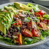 A vibrant Sweet Potato and Black Bean Bowl garnished with cilantro and lime wedges on a bed of greens.