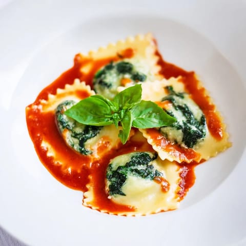 A steaming plate of spinach ricotta ravioli garnished with basil and Parmesan cheese.