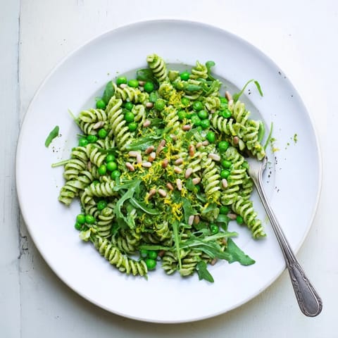 A close-up view of Spring Green Pesto Pasta Salad garnished with toasted pine nuts and lemon zest, perfect for spring picnics or potlucks.  