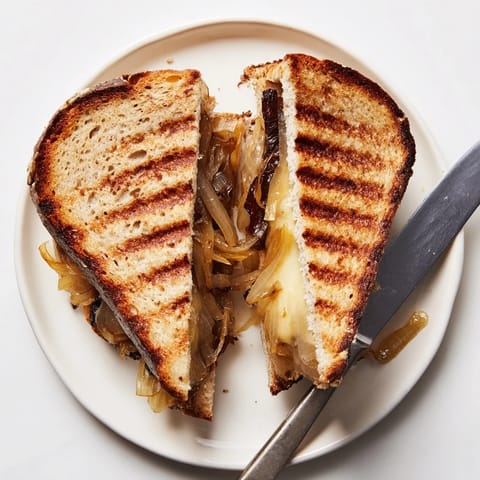 Golden caramelized onions and melted Gruyère cheese ooze from a perfectly grilled sandwich on a rustic plate.  