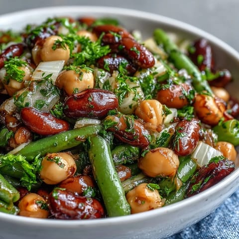 The Three-Bean Salad is tossed with fresh parsley and diced red onion, served chilled on a picnic table next to a rustic wooden spoon.  
