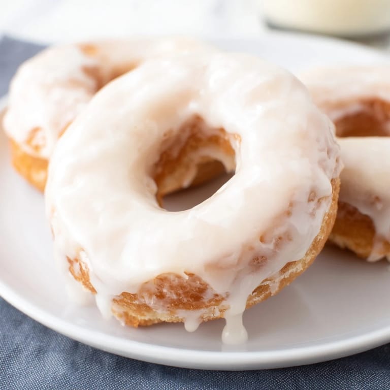 Warm, glazed yeast donuts glistening with icing, offering a soft aroma and sweet, irresistible flavor.