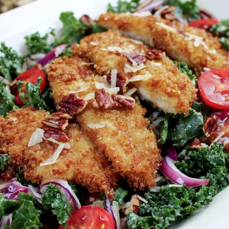 The Crispy Chicken Kale Salad showcases crispy chicken atop massaged kale, finished with Parmesan and a sweet, tangy dressing.
