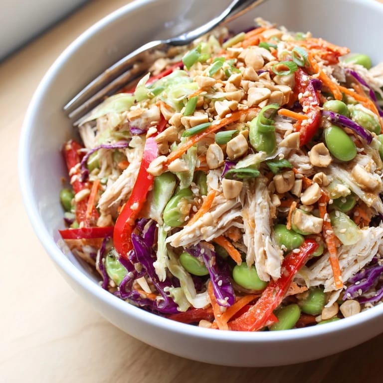 A vibrant bowl of Edamame Crunch Chicken Salad with carrots, red bell pepper, and toasted sesame seeds.