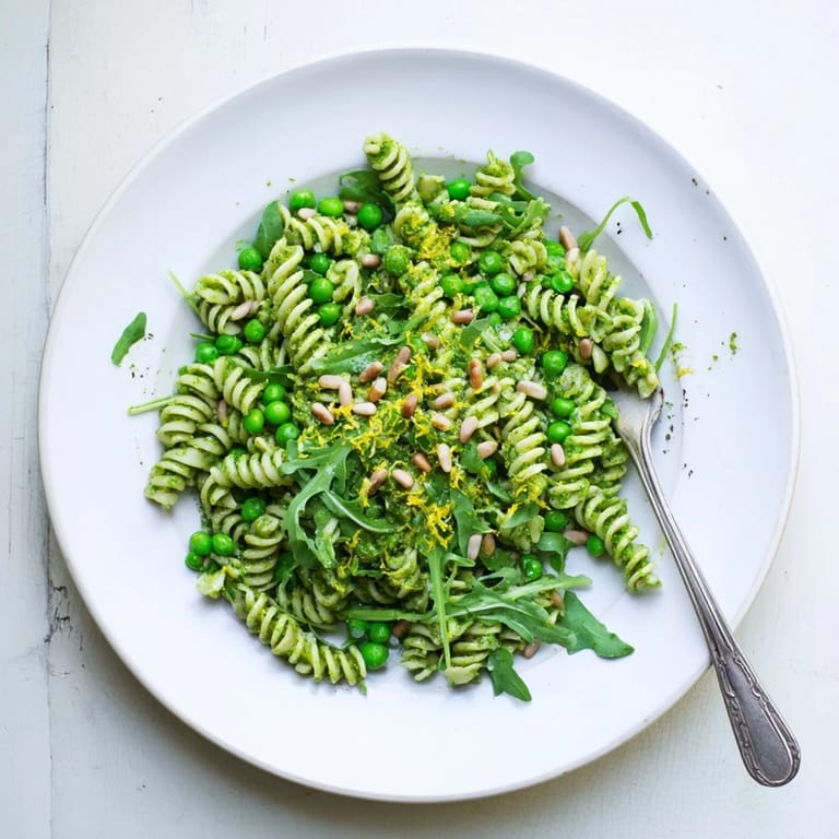 A close-up view of Spring Green Pesto Pasta Salad garnished with toasted pine nuts and lemon zest, perfect for spring picnics or potlucks.  