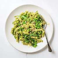 This Spring Green Pesto Pasta Salad features al dente pasta coated in bright basil pesto, sweet peas, and peppery arugula for a refreshing bite.  