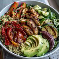 Golden pan-fried chicken and paprika roasted vegetables on fluffy quinoa topped with avocado and a lemon salad.