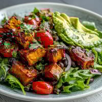 Roasted sweet potatoes and black beans in a bowl with avocado and fresh salsa, drizzled with zesty lime dressing.